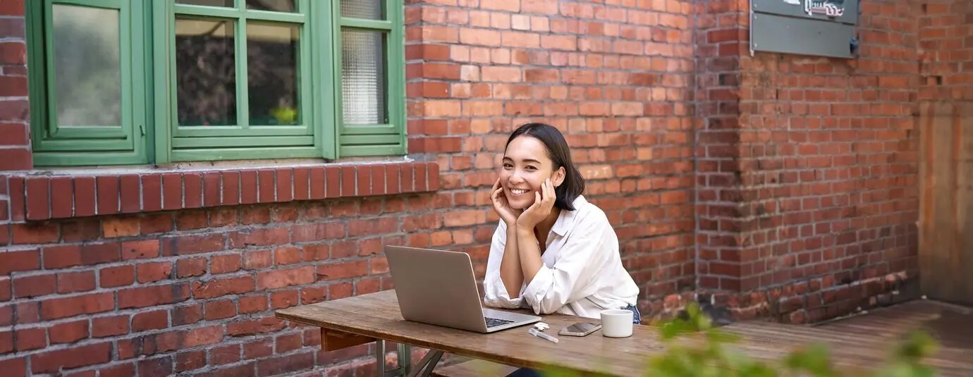Schöne brünette Frau sitzt draußen und benutzt einen Laptop, chattet online und arbeitet am Computer.